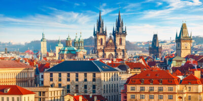 High spires towers of Tyn church in Prague city (Church of Our Lady before tyn cathedral) urban landscape panorama with red roofs of houses in old town and blue sky with clouds